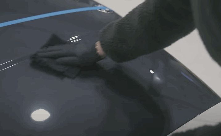A gloved hand applies ceramic coating to the hood of a car along a blue tape line, enhancing its shine and smoothness.