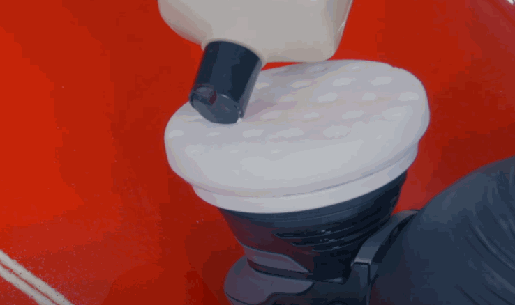 Polishing compound is applied to a dual-action buffer pad before polishing a red vehicle’s surface as part of the paint protection film prep process.