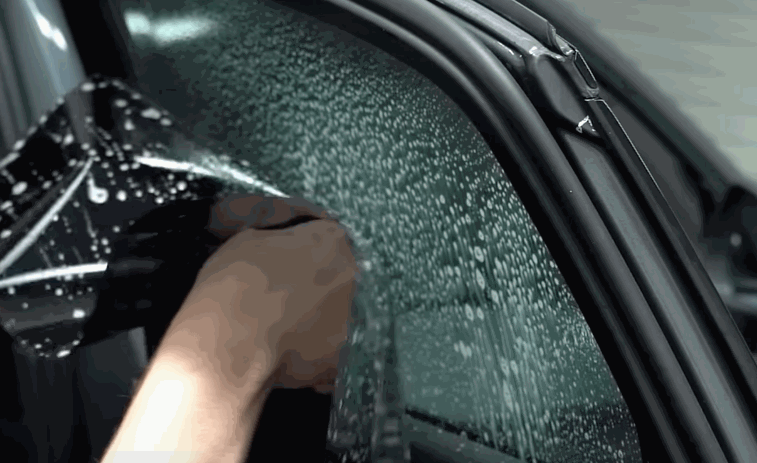 Installer positioning window tinting film onto a wet car window for proper adhesion.