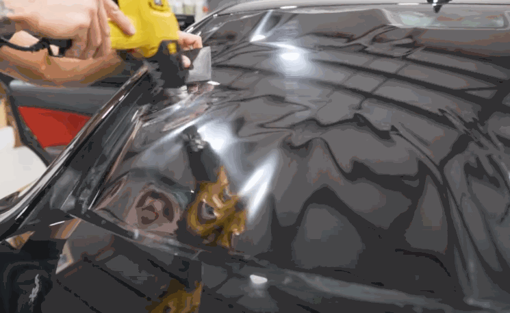 Technician using a heat gun to shrink and mold window tinting film on a car’s rear window.