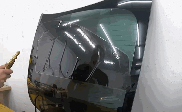 Applying heat to smooth out freshly installed window tinting film on a detached car window.
