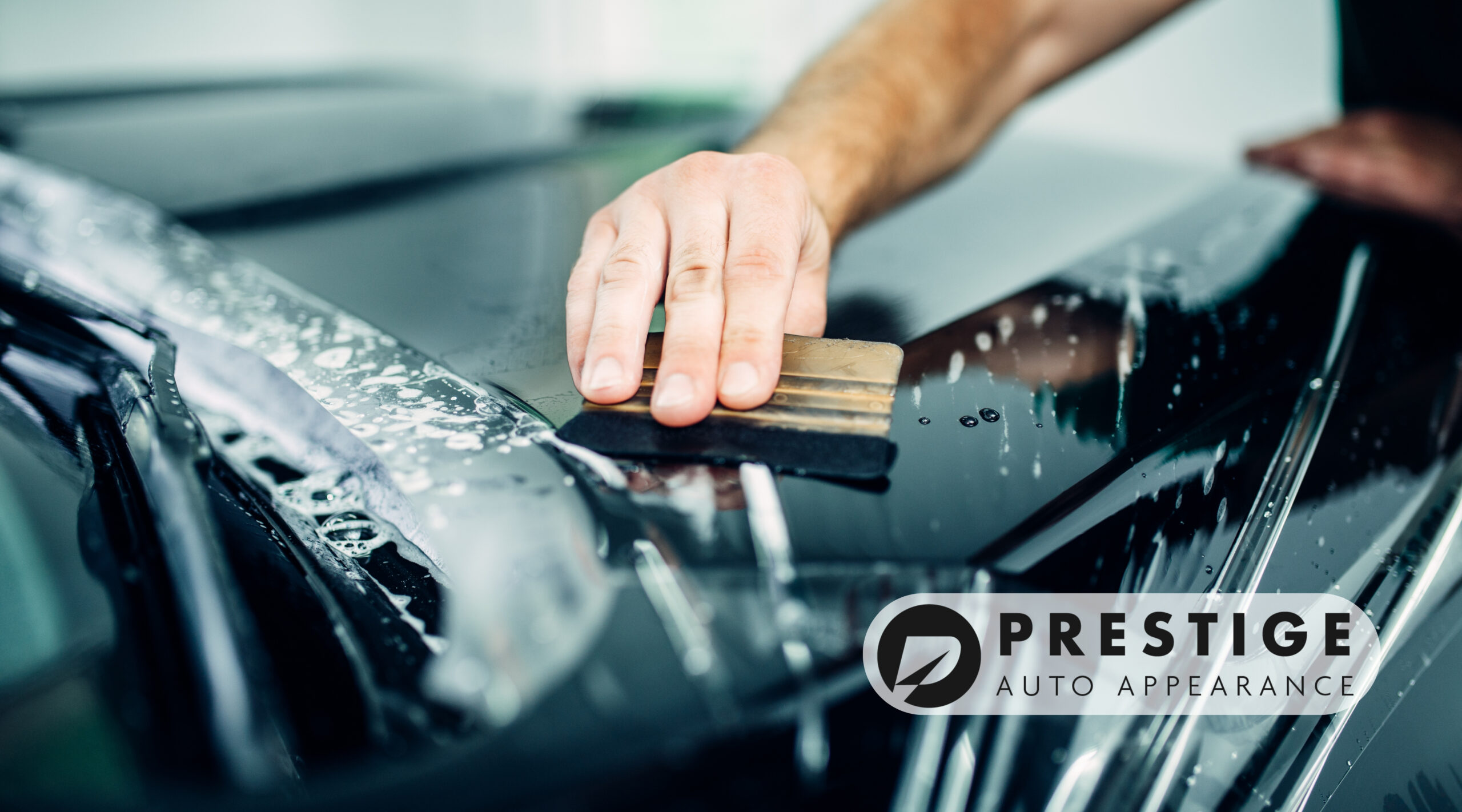 Close-up of a professional applying a protective film to a car’s surface.