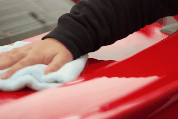 Close-up of a Prestige Auto Appearance technician wiping a red car’s surface with a microfiber cloth for a spotless finish.