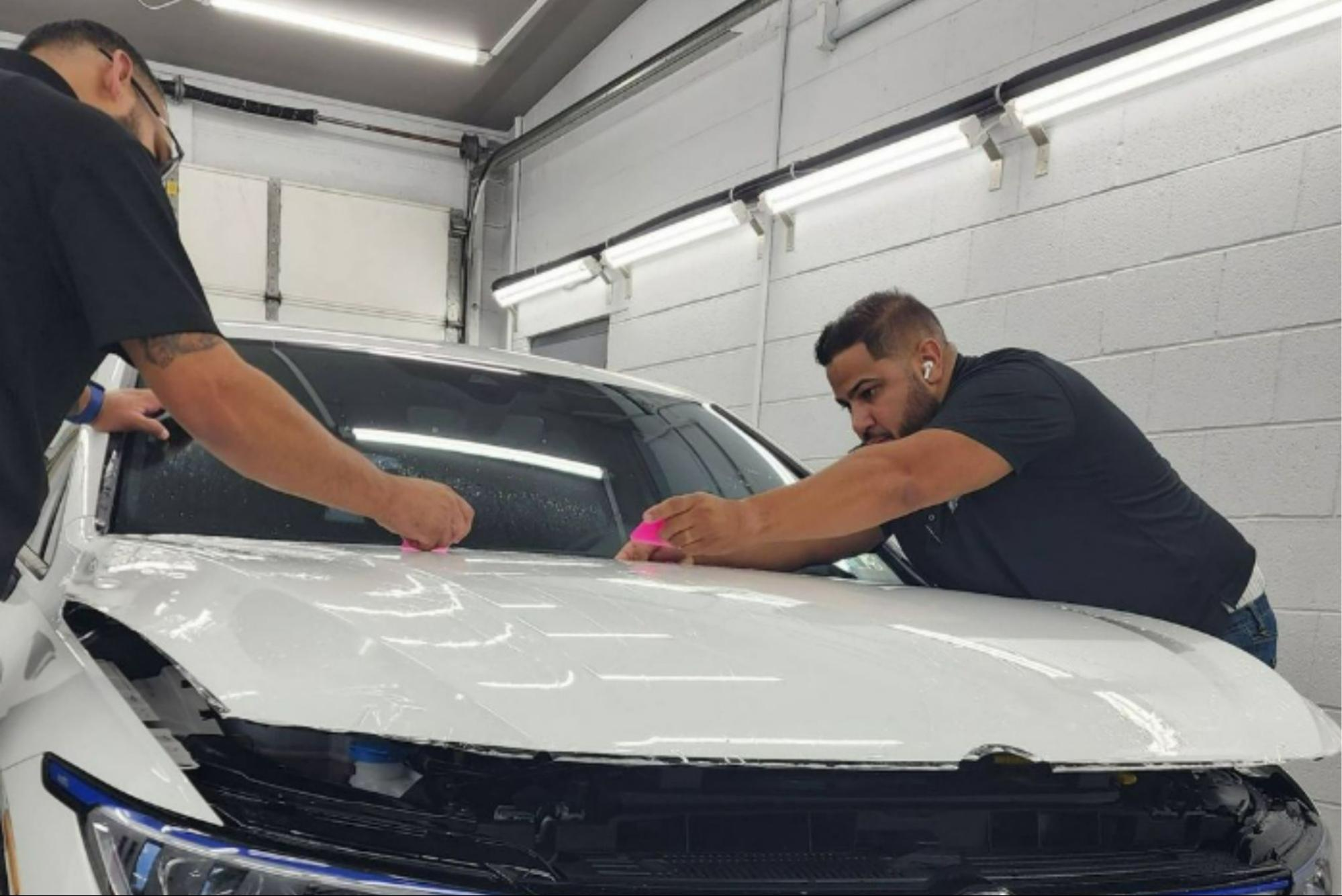 Prestige Auto Appearance experts applying paint protection film (PPF) on a white vehicle’s hood.