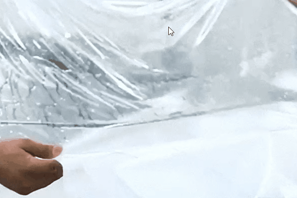 Technician installing clear paint protection film on a vehicle in a professional detailing shop.