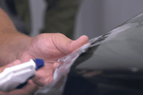 Close-up of a technician applying paint protection film by hand to a vehicle surface.