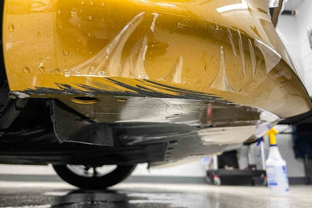 Close-up of damaged paint protection film on a yellow bumper, showing how PPF prevents scratches and chips from reaching the paint.