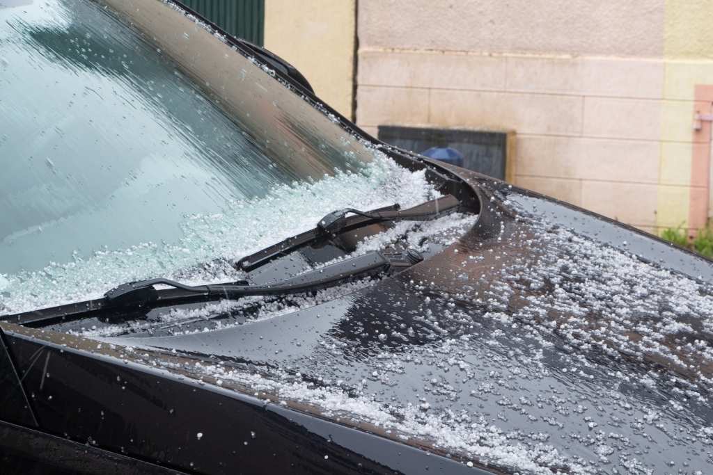 Car windshield and hood covered in ice pellets and slush, showing the effects of harsh winter weather on vehicle surfaces.