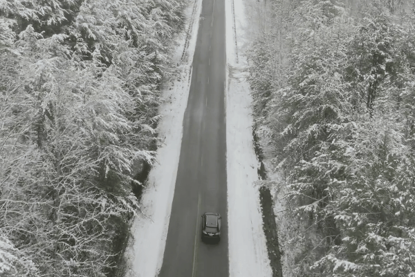 Car driving on a snow-lined road through a winter forest, highlighting harsh conditions that impact vehicle paint.