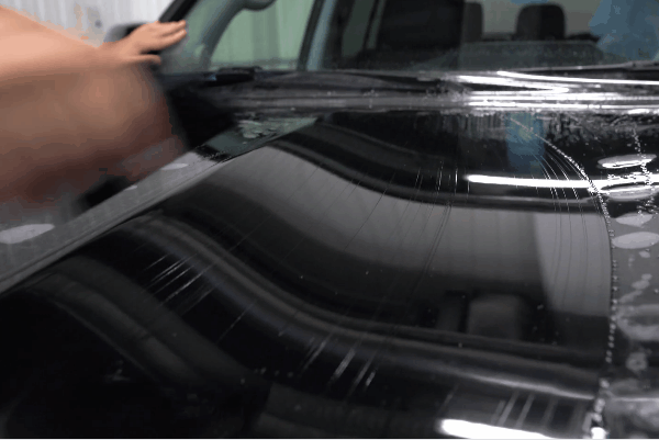 Close-up of technician applying paint protection film to a car hood for winter paint protection and surface durability.