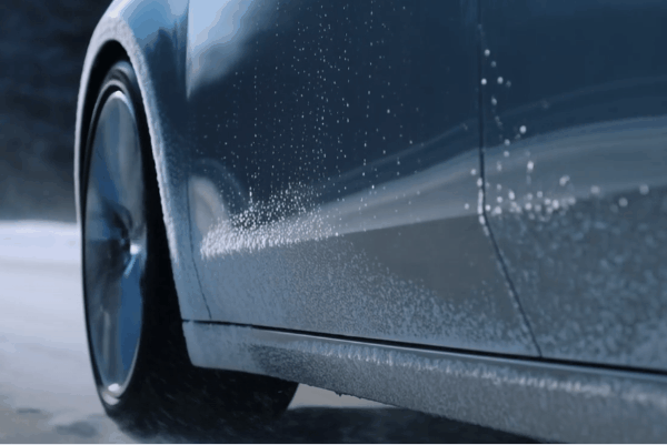 Car driving through snow with road salt splashing along the side panels during winter.