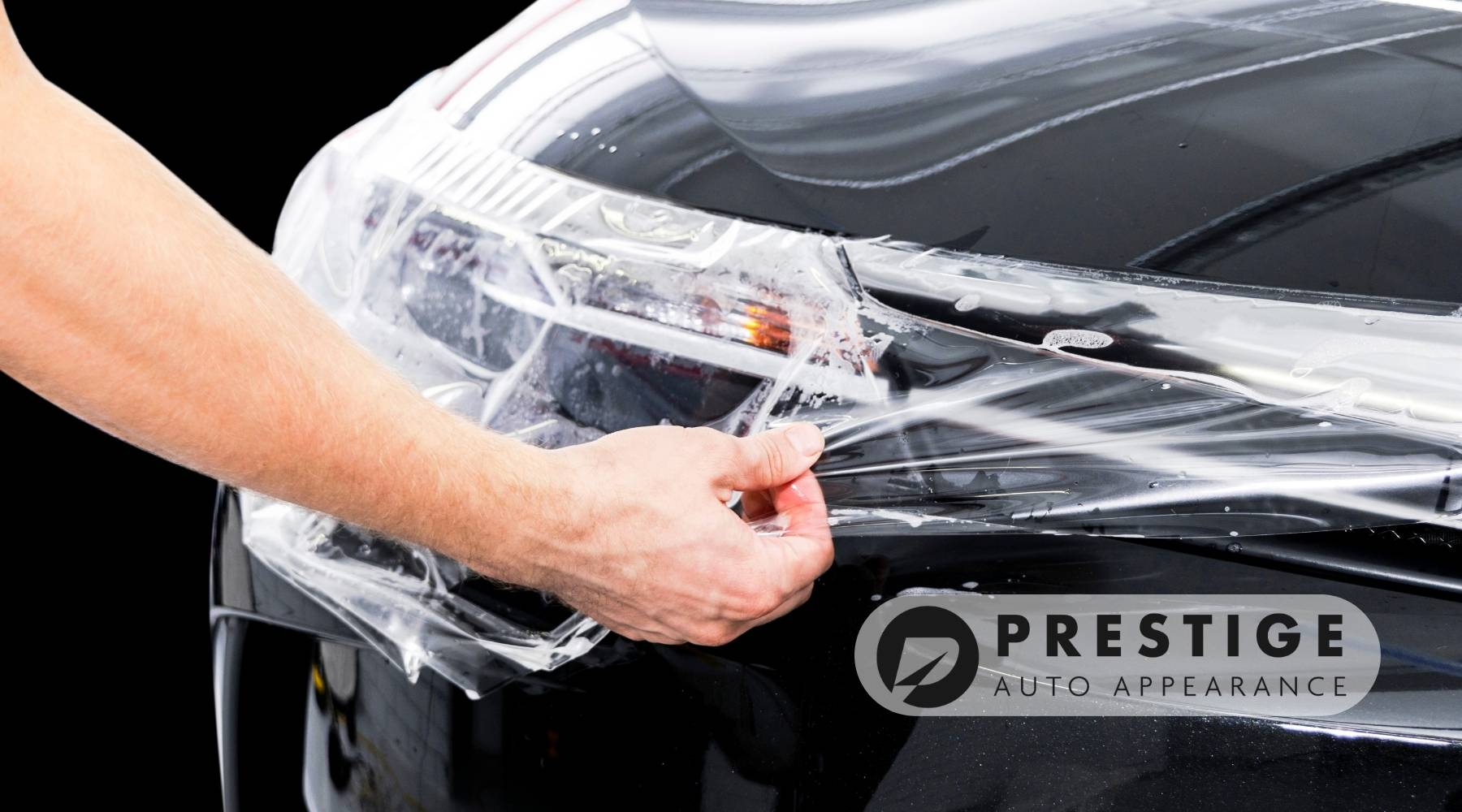 Technician applying paint protection film to a car’s headlight and fender at Prestige Auto Appearance.