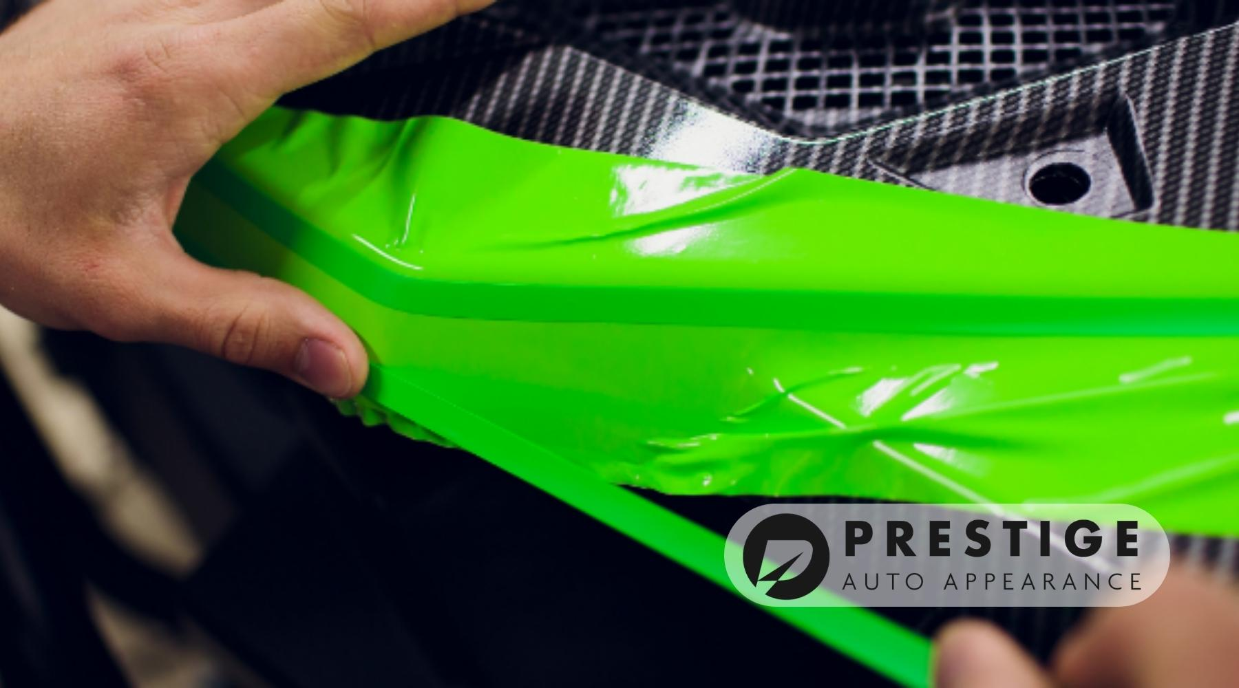Hands applying a bright green vinyl wrap to a car panel with a carbon fiber texture at Prestige Auto Appearance in Allentown, PA.