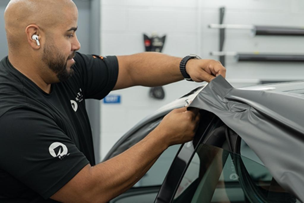 Prestige Auto Appearance technician applying a gray vinyl wrap to the roofline of a car inside the Allentown studio.