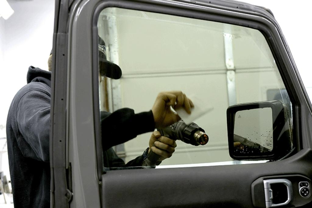 Technician installing ceramic window tint on a car door using a heat gun