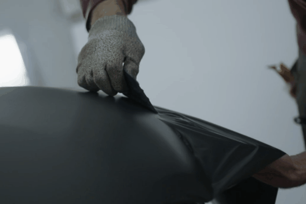 A technician wearing gloves carefully installing a matte black vinyl wrap on a vehicle at Prestige Auto Appearance.