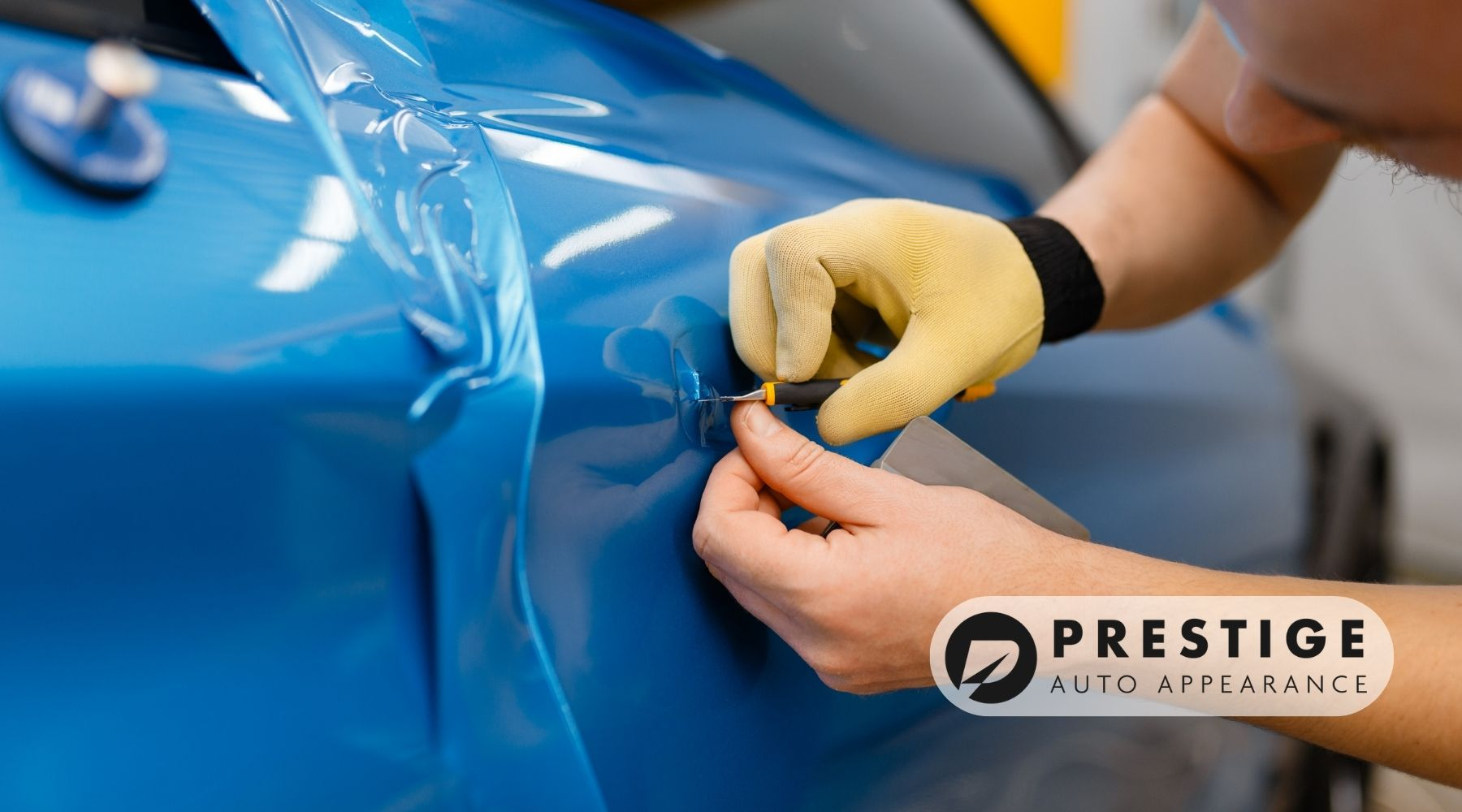 Technician applying a blue vinyl wrap to a car door with precision tools at Prestige Auto Appearance