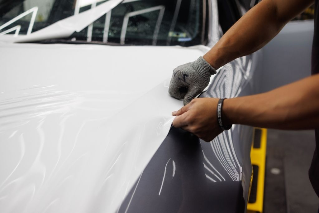 Installer applying white vinyl wrap over a dark-colored vehicle during a professional wrap installation.