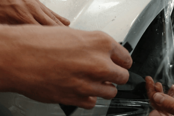 Close-up of technician applying paint protection film to a vehicle panel for chip and scratch protection.