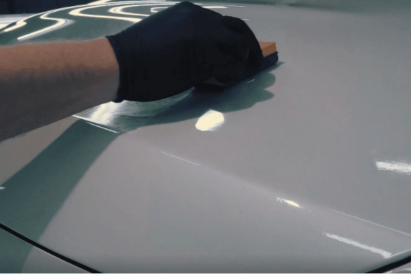 Close-up of a technician wearing a black glove applying ceramic coating to a white vehicle surface inside a professional auto detailing studio.