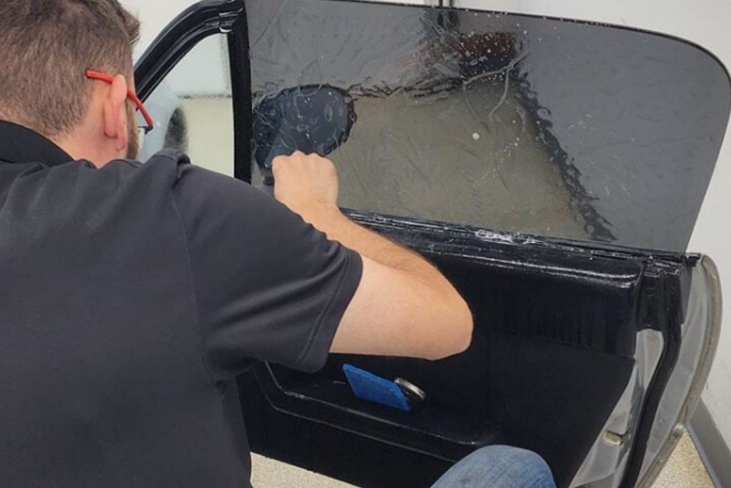 Technician installing window tint film on a car door window during a professional tint application