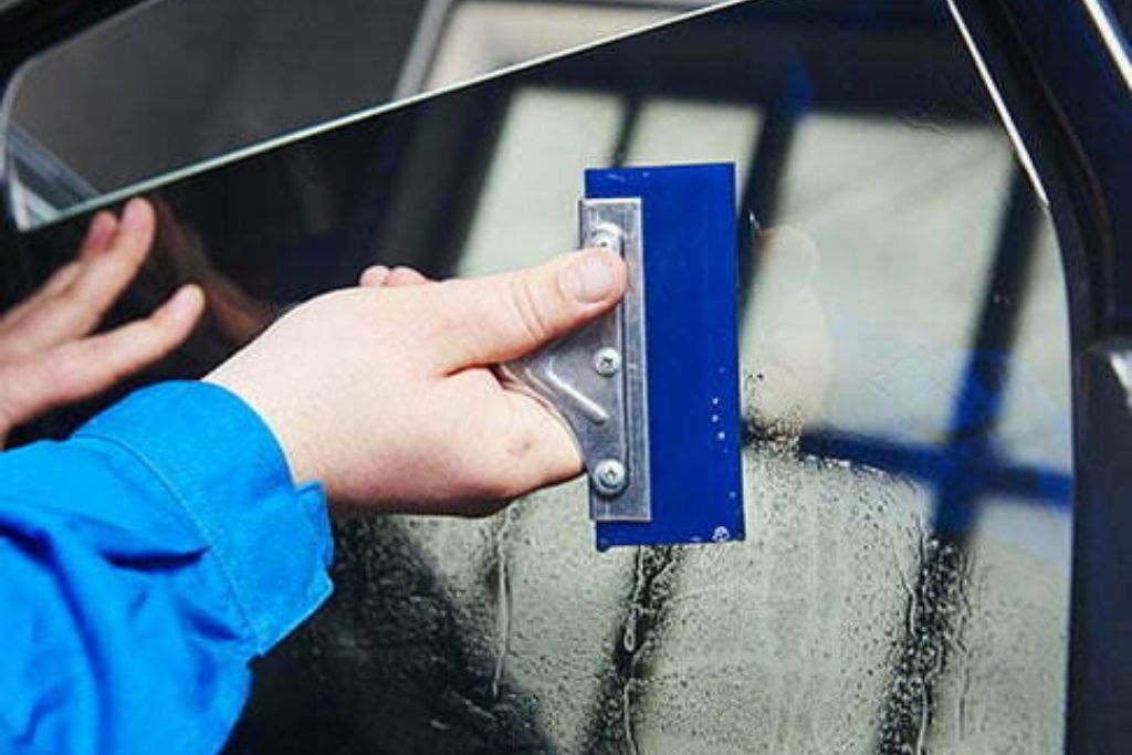 Technician smoothing window tint film onto a car door window during installation