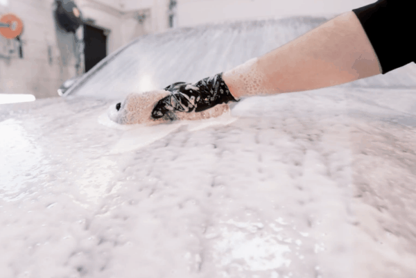 Detailing technician hand washing a car covered in foam during a professional exterior car detailing service.