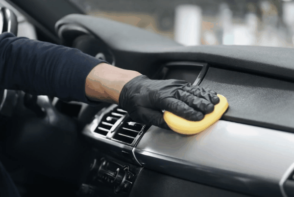 Detailing professional cleaning a car dashboard with a microfiber applicator during interior auto detailing.