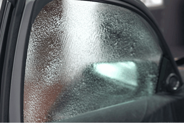 Close-up of a car side window with moisture trapped beneath freshly applied window tint film