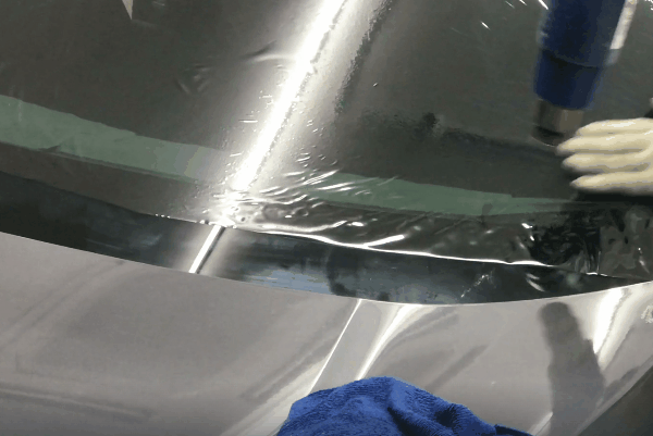 Close-up of window tint film being heat-shaped on a car rear window during installation