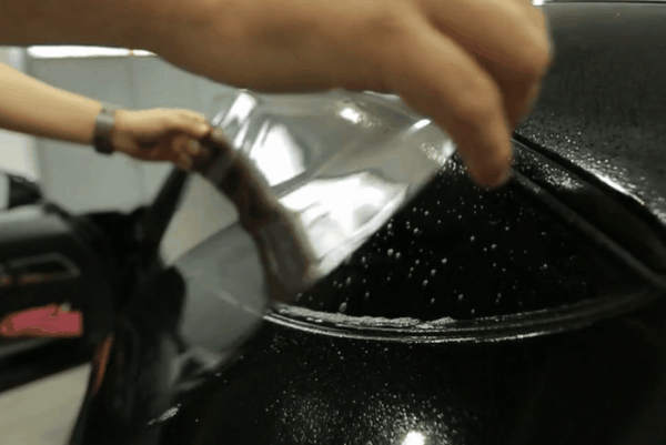 Technician peeling window tint film from a wet vehicle window during the tint installation process.