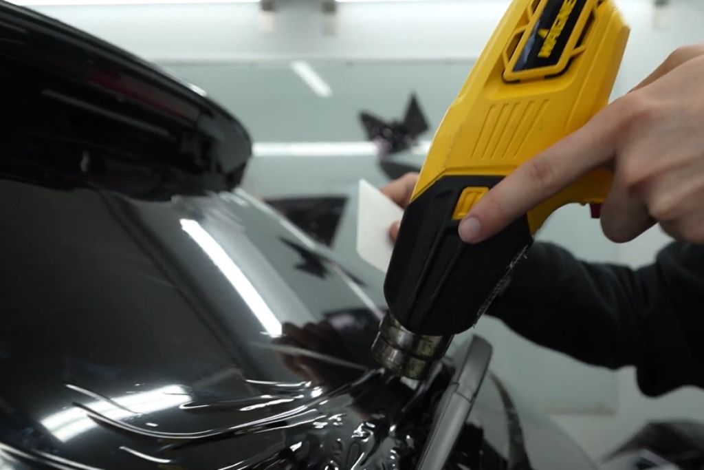 Technician using a heat gun to shape window tint film on a vehicle’s rear window.