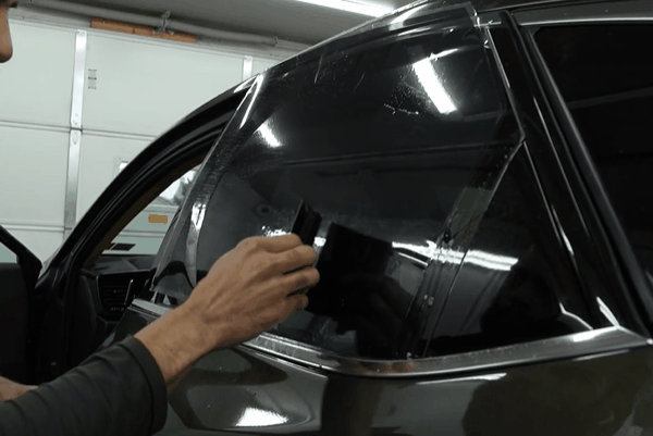 Technician smoothing window tint film onto a vehicle’s rear side window during installation.