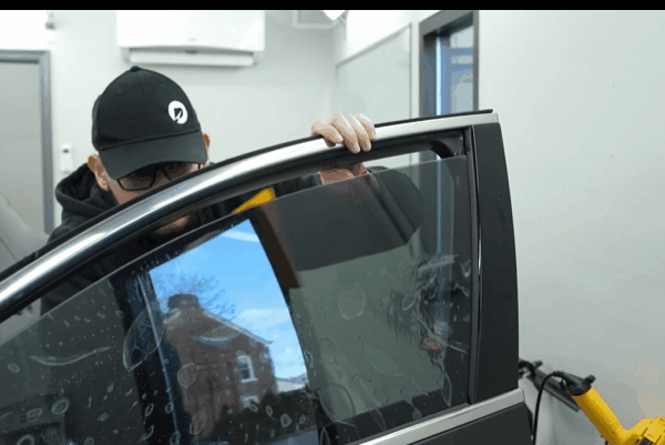 Technician installing window tint film on a car door window at an automotive appearance shop.