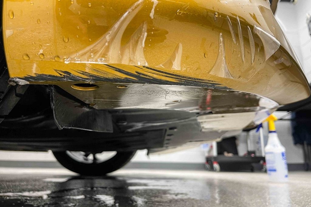 Paint protection film being applied to the lower panel of a yellow vehicle for rocker panel and road debris protection.