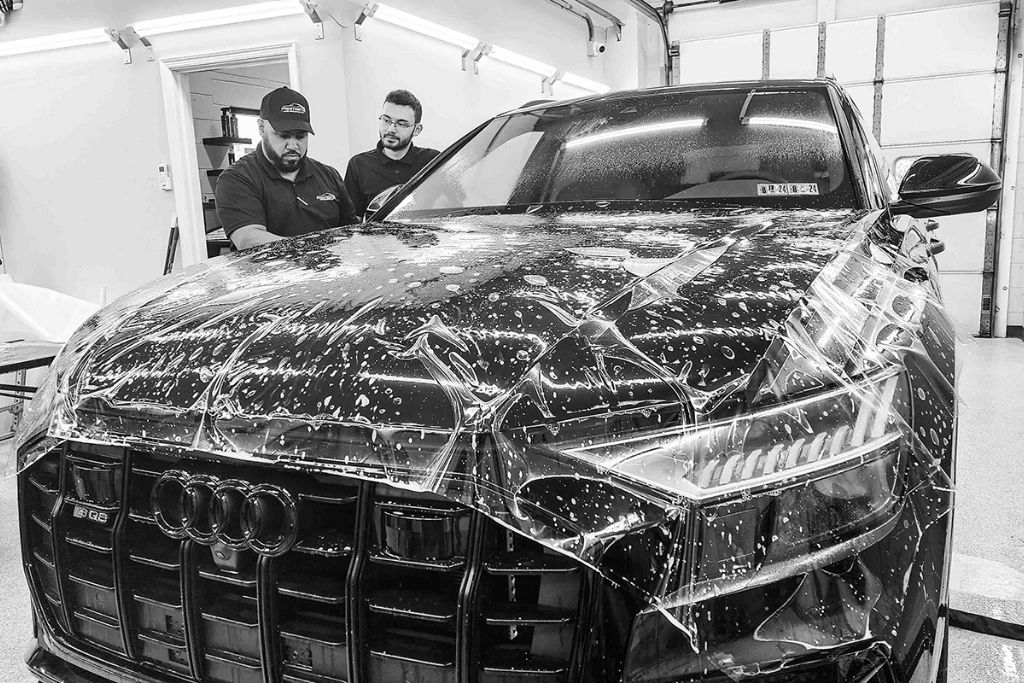 Prestige Auto Appearance technicians installing paint protection film on the front end of a black Audi SUV.
