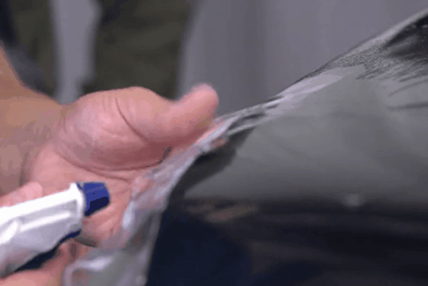 Technician applying paint protection film to the edge of a black vehicle panel using slip solution for a smooth fit.