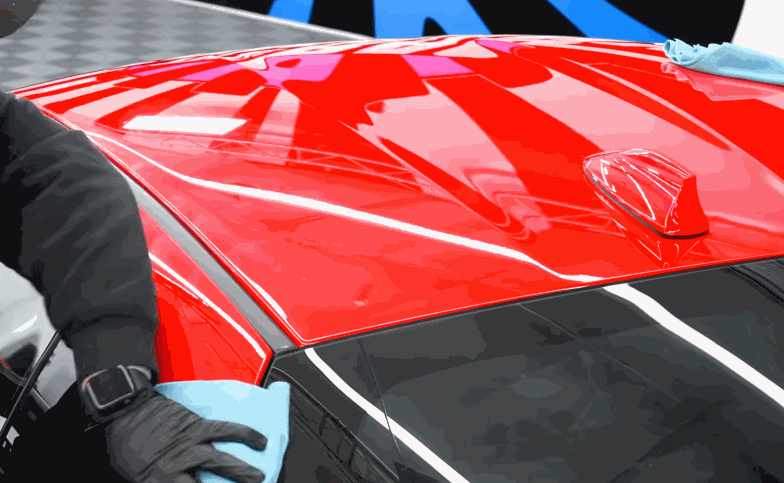 Technician wipes ceramic coating across the glossy red roof of a car with a blue microfiber cloth nearby.