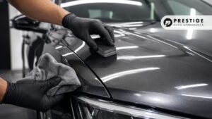 Technician applies ceramic coating to a gray car hood with an applicator pad and microfiber towel.